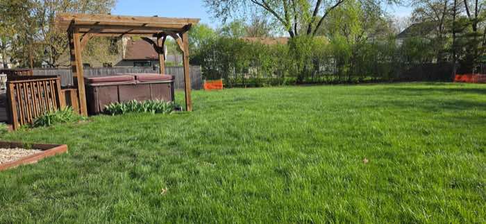 Back lawn with long, overgrown grass beside a wooden pergola and hot tub